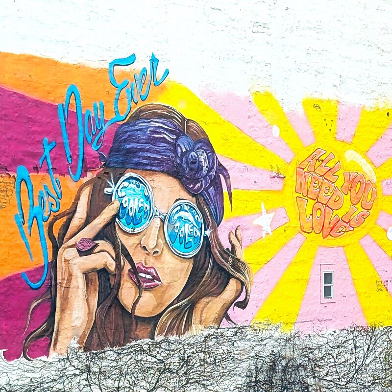 Downtown Toledo mural at Adams and Superior featuring a woman in sunglasses with 'Best Day Ever' script and an 'All You Need Is Love' sunburst